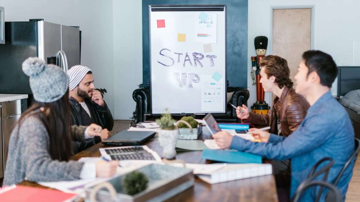 Startup team planning growth ideas around a table with laptops and a whiteboard
