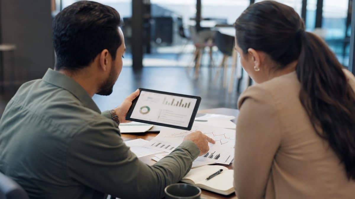 Two colleagues reviewing analytics charts on paper and a tablet during a planning discussion